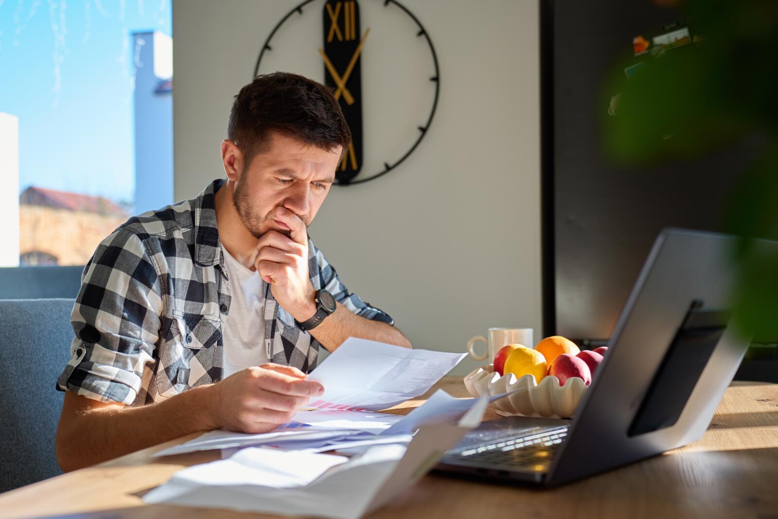 Worried,Man,Checking,Bills,And,Financial,Papers,While,Sitting,At
